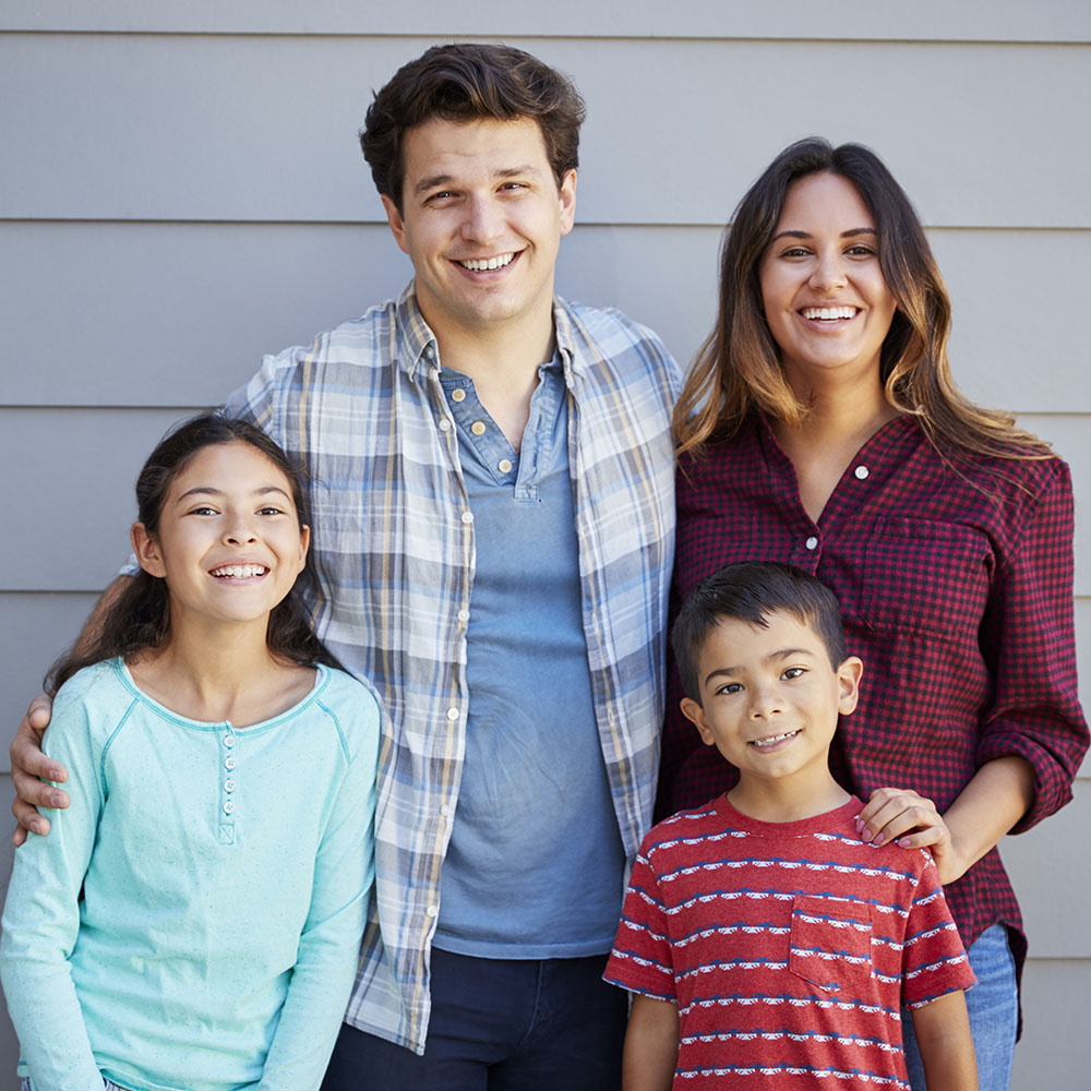 Portrait Of Happy Family Standing Outside Grey Clapboard House